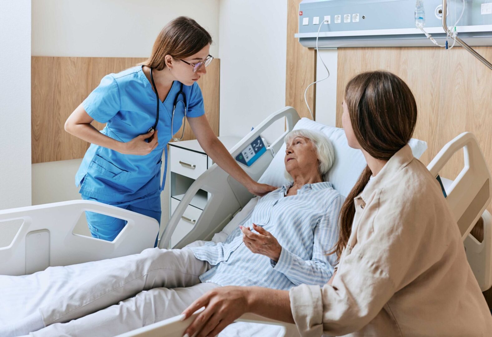 Nurse and visitor with elderly patient in hospital.